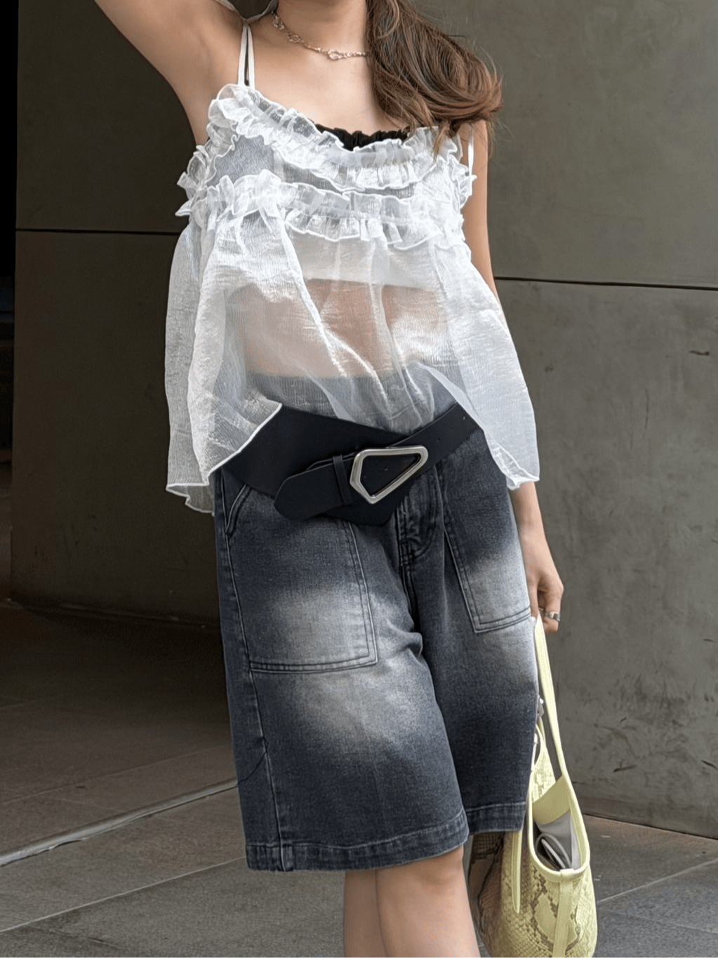 Chrome Phase belt with an angular buckle, a sheer white ruffled top and charcoal denim shorts