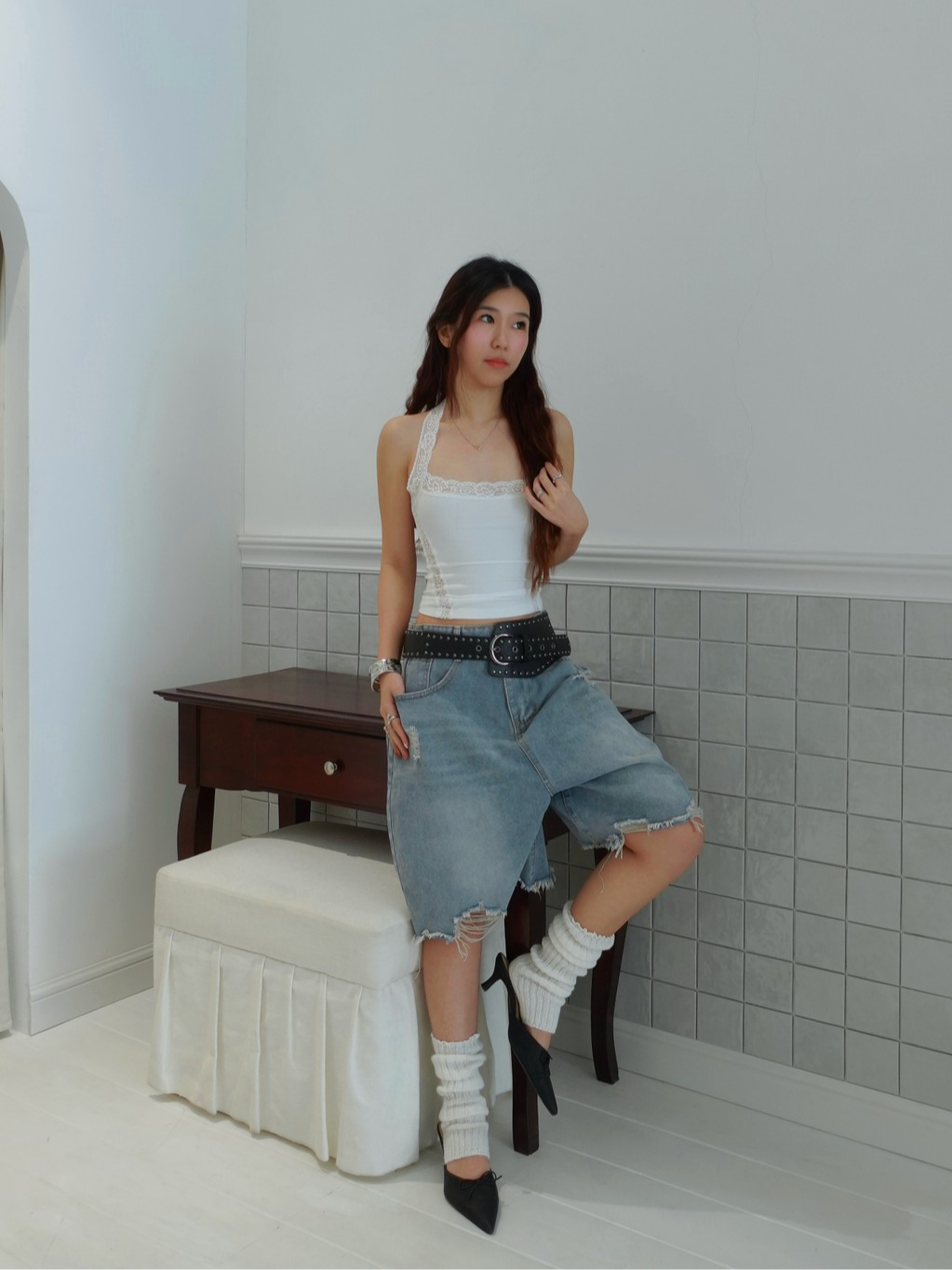 Pure Noise black studded belt with a white lace-trim top, loose denim shorts and pointed black heels
